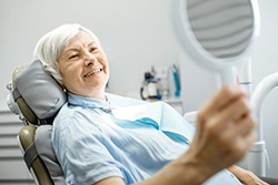older woman in dental chair smiling while looking into mirror