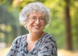 Senior woman sitting outside and smiling with dentures in Syracuse, NY