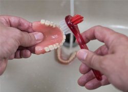 Close-up of cleaning dentures in Syracuse, NY with a brush