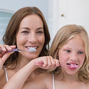 Mother showing daughter how to brush teeth