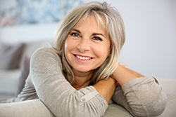 Woman I grey shirt smiling with arms crossed over couch