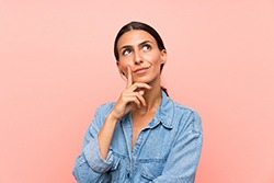 Woman with hand on her chin thinking with pink background