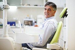 Man smiling in dental chair wearing collared shirt