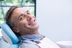 Man smiling in dental chair while wearing a light blue collared shirt