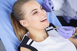 Woman in dental chair smiling while wearing white and black top