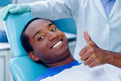 Man in blue shirt smiling in dental chair with thumb up